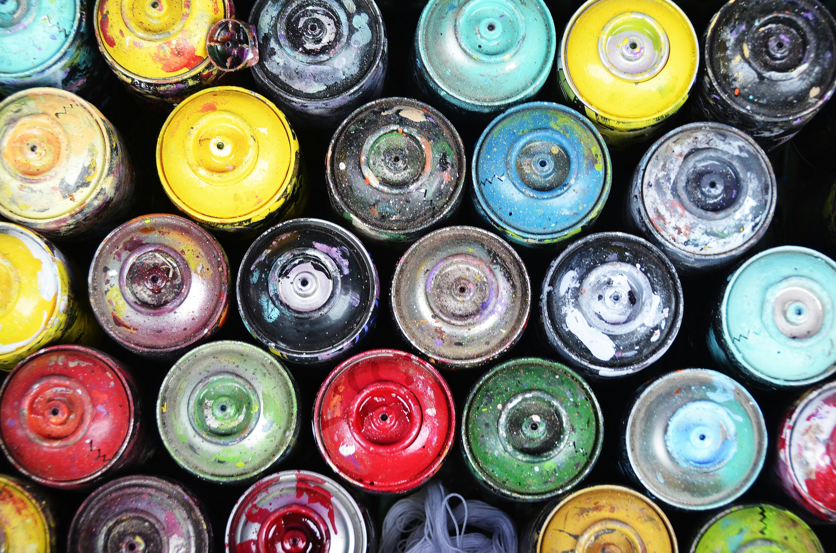 An overhead arrangement of brightly coloured, paint-splattered spray cans