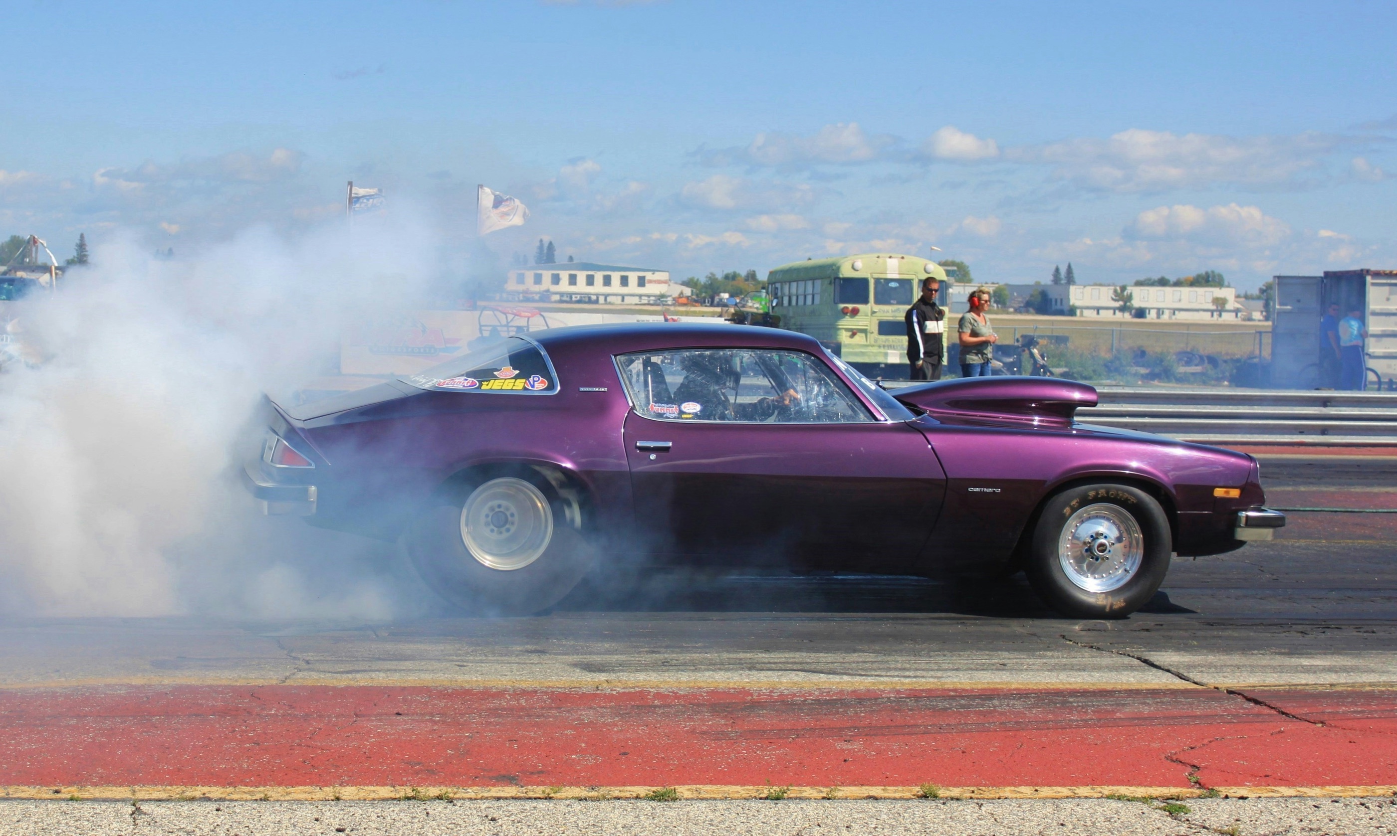A purple drag-racing car doing a smoky burnout beneath a blue sky