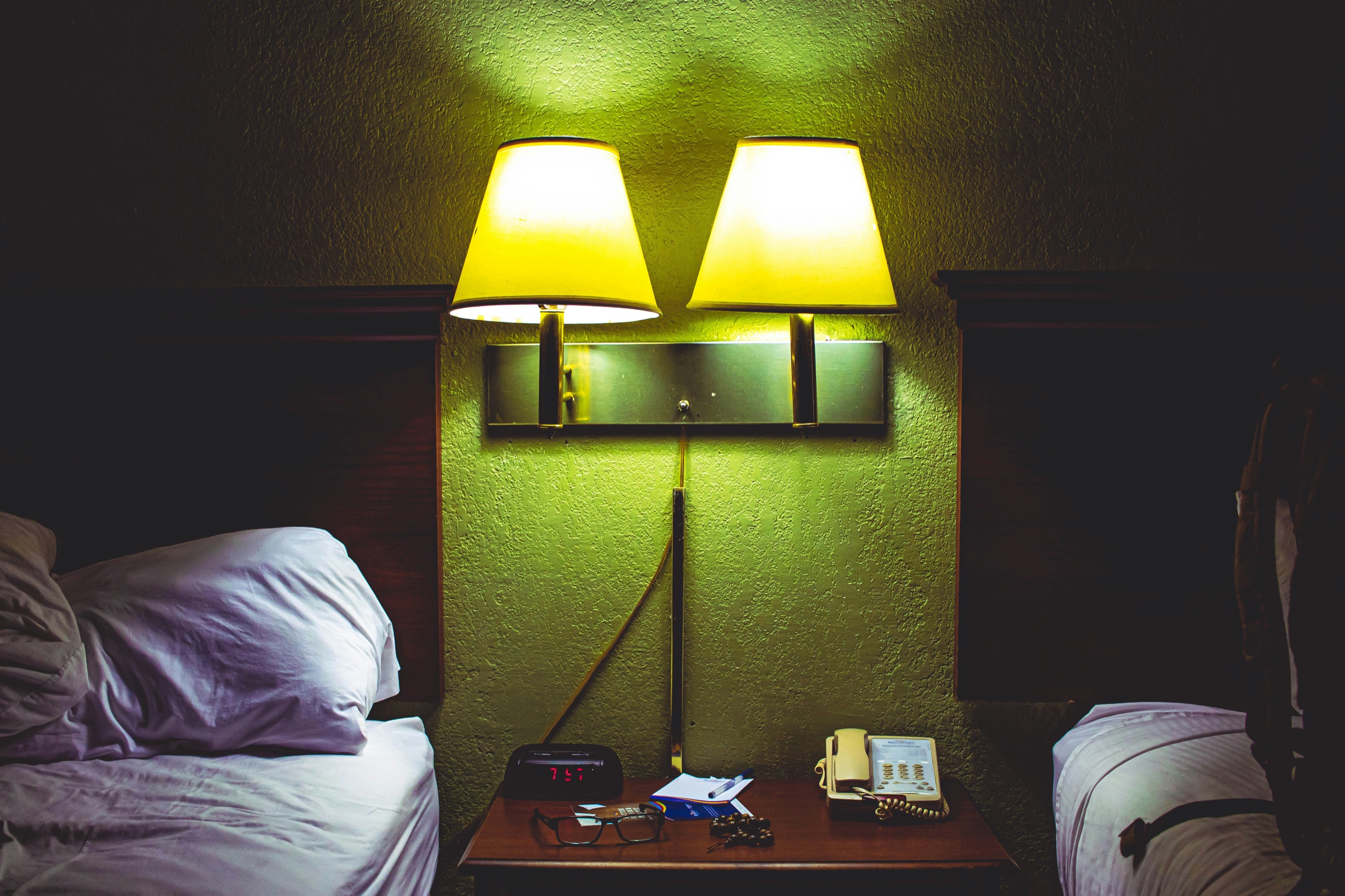 Two glowing bedside lamps between the beds in a dark motel room